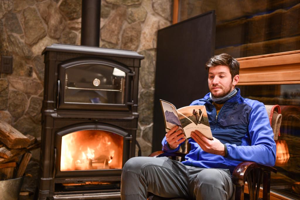Mann liest neben einem Holzofen im Chalet